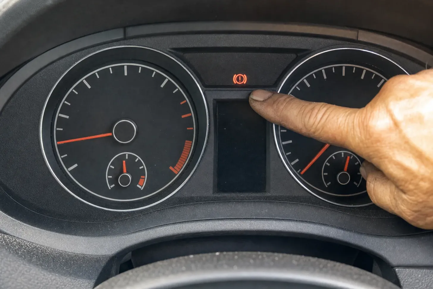 Finger pointing at a lit brake warning light on a car dashboard