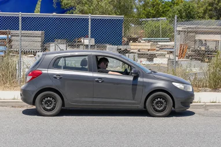 Driver in the seat of a grey hatchback parked at the kerb, door open