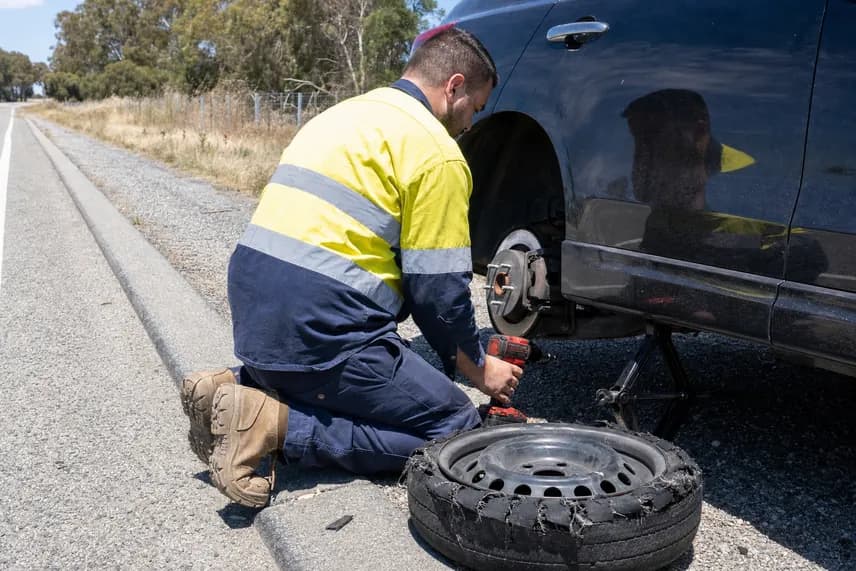 Roadside worker fitting the spare after a blowout, the shredded tyre on the ground beside him