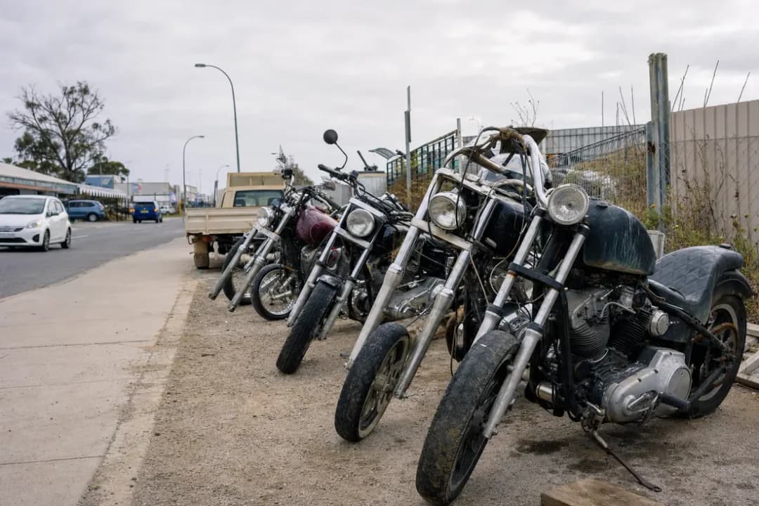 Row of custom motorcycles parked in a lot under a cloudy sky.