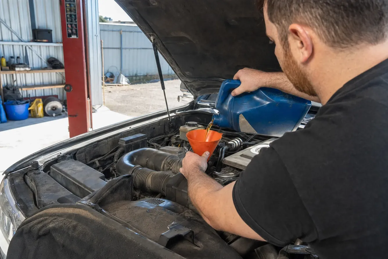 Engine oil being topped up through a funnel under an open bonnet