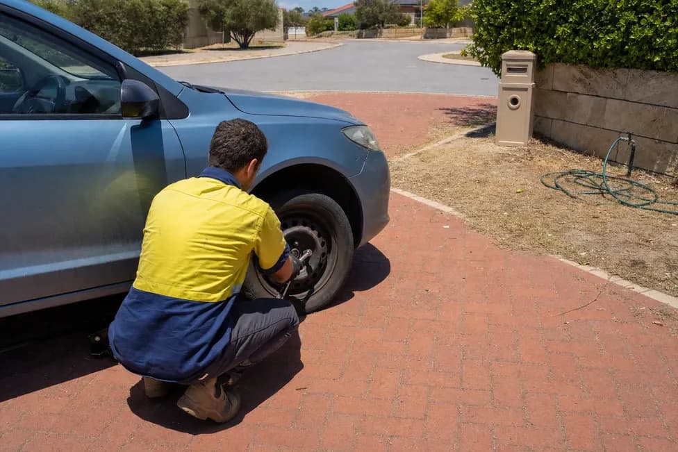 Man working on the front wheel of a blue hatchback in a driveway