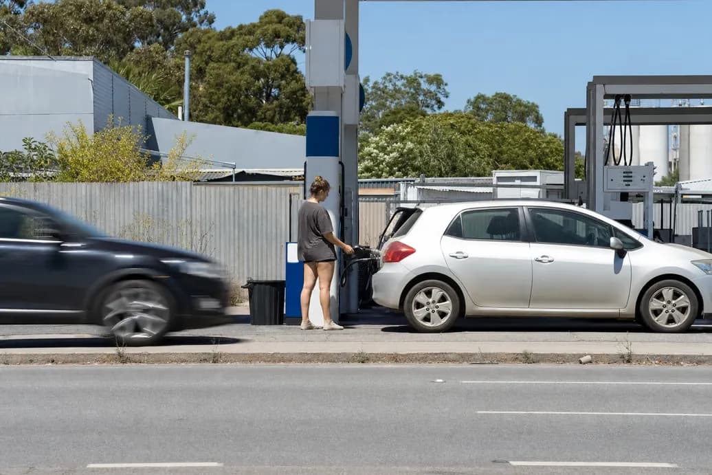 Woman filling up a silver hatchback at a service station