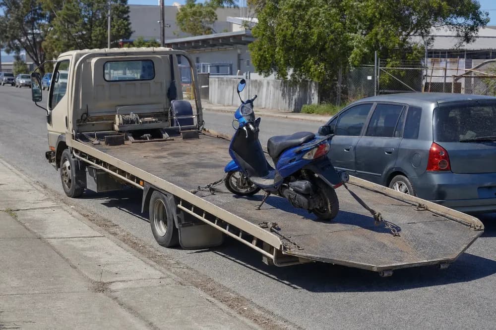 Blue moped scooter parked on a city street curb next to a car, ready for transport.