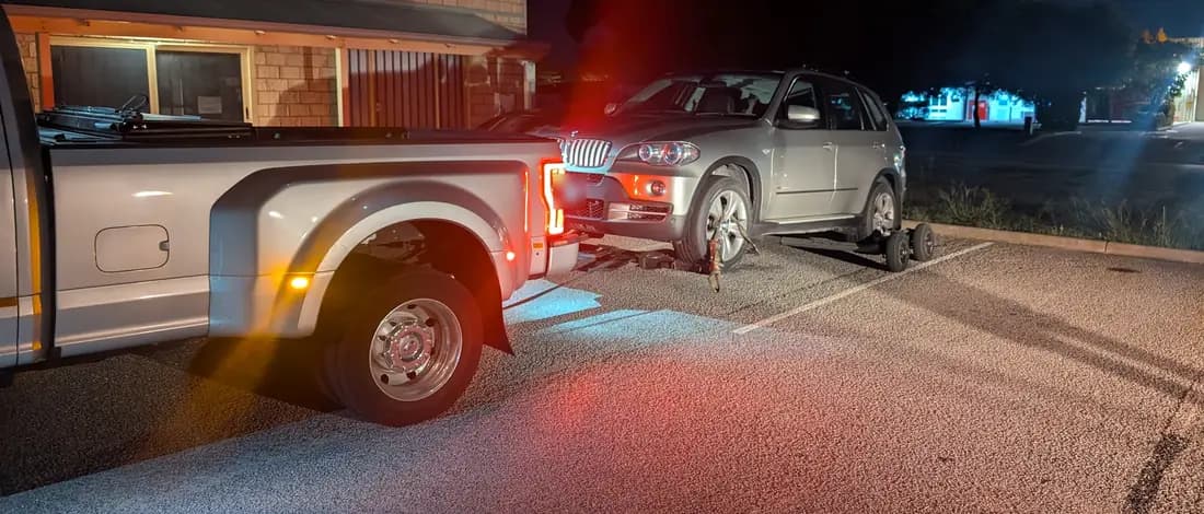 Silver BMW X5 on the wheel lift behind the Quokka Towing dual-wheel Ford at night in Kwinana
