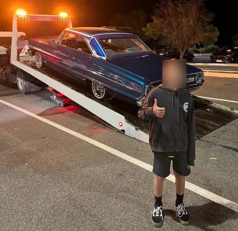 Young passenger gives a thumbs up in front of a blue 1964 Ford Galaxie loaded on a tilt tray at night