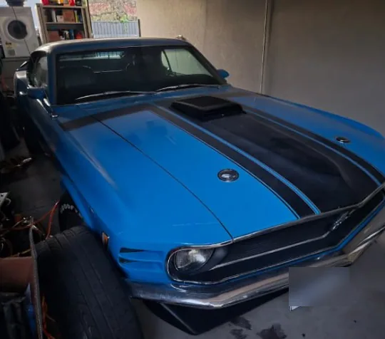 Blue 1970 Ford Mustang fastback with black stripes and bonnet scoop, home in the garage after the tow
