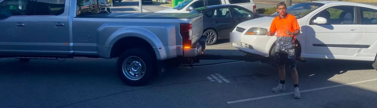Customer in hi-vis gives a thumbs up beside his white Holden Barina on the Quokka Towing wheel lift
