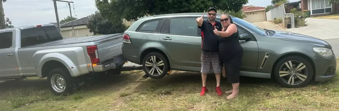 Couple give a thumbs up beside their grey Holden Commodore wagon on the Quokka Towing wheel lift