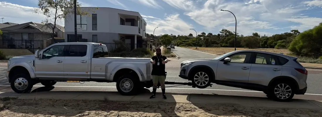 Quokka Towing driver gives two thumbs up between the dual-wheel Ford and a silver Mazda CX-5 on the wheel lift in Bertram