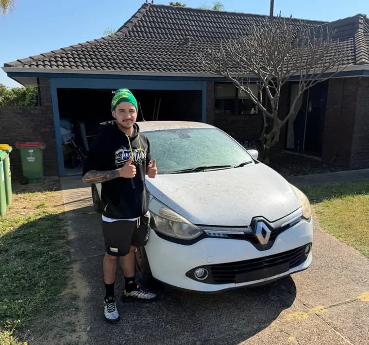 Customer gives two thumbs up beside his white Renault Clio, towed back home to his driveway in Yanchep