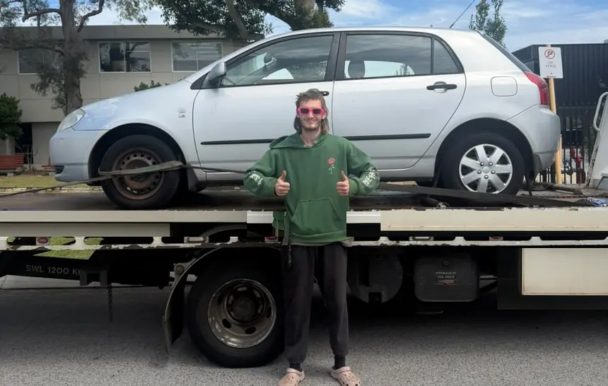 Customer in sunglasses gives two thumbs up in front of his silver Toyota Corolla strapped down on a tilt tray