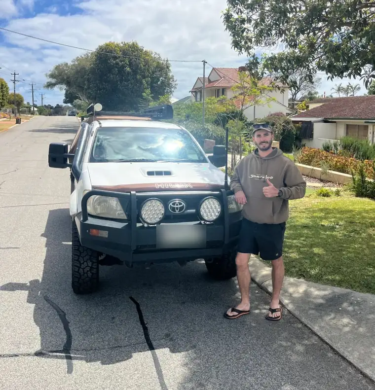 Repeat customer gives a thumbs up beside his white Toyota HiLux with bullbar and snorkel, parked back home after the mechanic