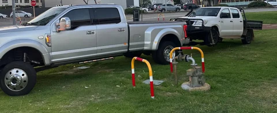 White Toyota HiLux tray ute on the wheel lift behind the Quokka Towing dual-wheel Ford, parked on the grass in Como