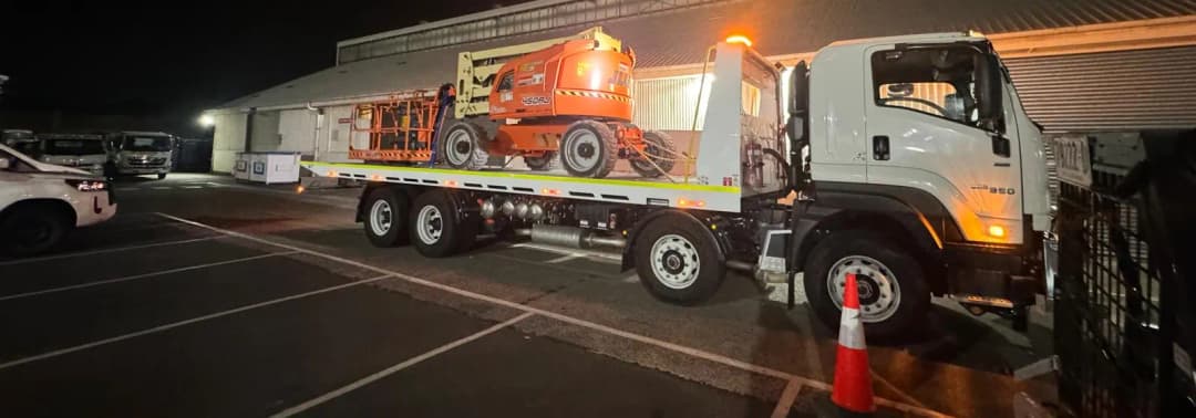 Boom lift loaded on a Quokka Towing truck at night