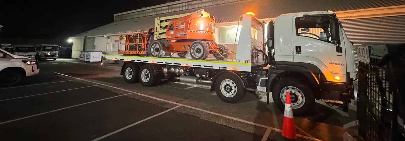 A Quokka Towing tilt tray loaded with an orange boom lift at night