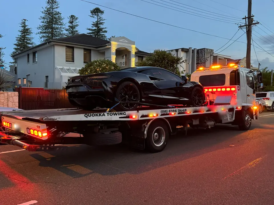 Black supercar strapped down on a Quokka Towing tilt tray at dusk