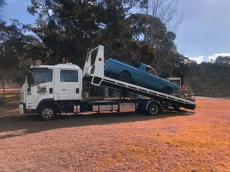 Tilt tray loading a classic blue ute on a rural block