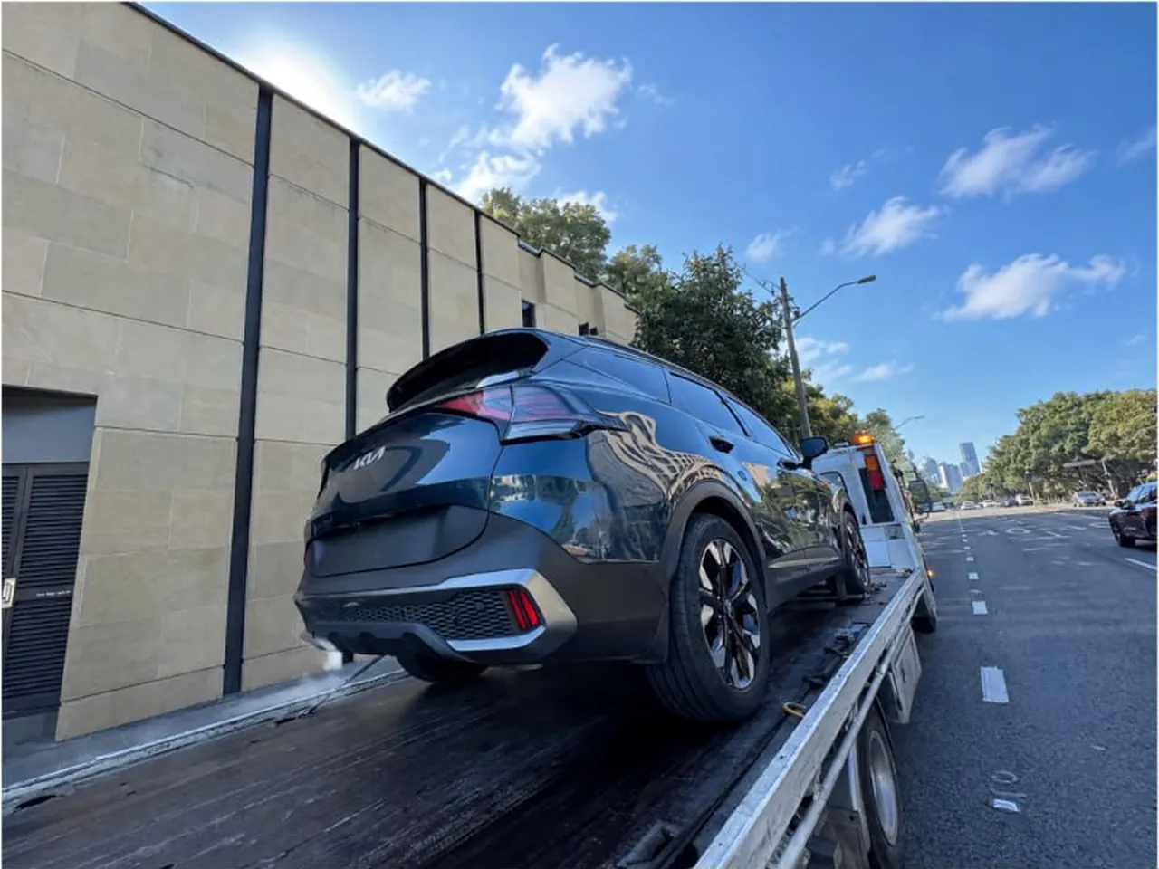 Quokka Towing tilt tray carrying a dark Kia SUV along a city street