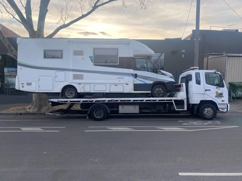 Quokka Towing tilt tray truck transporting a large white caravan in a suburban area.