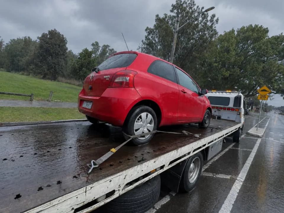 Quokka Towing tilt tray carrying a red Toyota Yaris strapped down in the rain