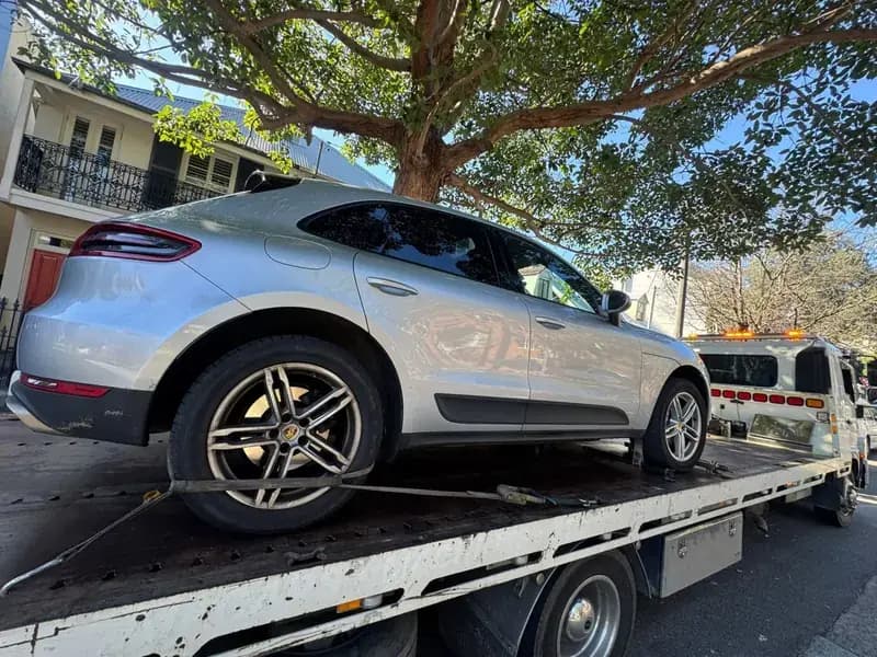 Quokka Towing tilt tray carrying a silver Porsche SUV under a street tree