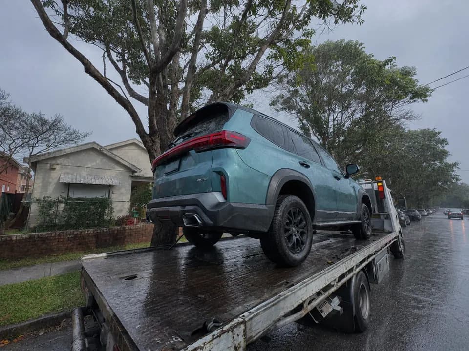 Quokka Towing tilt tray carrying a teal SUV on a wet residential street