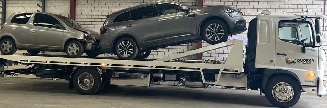 Quokka Towing tilt tray carrying two damaged cars, one raised on the upper deck