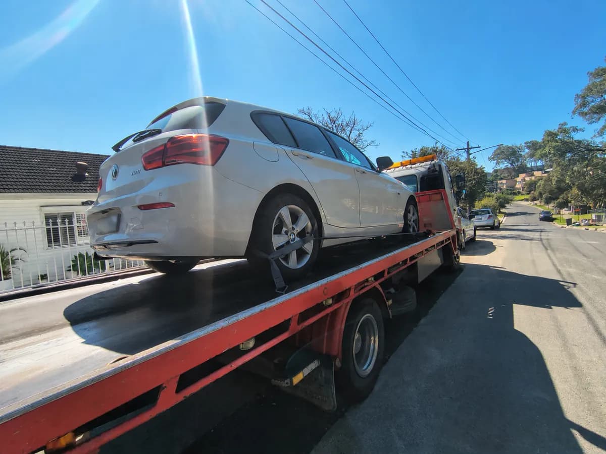 Tilt tray carrying a white BMW hatchback along a residential street