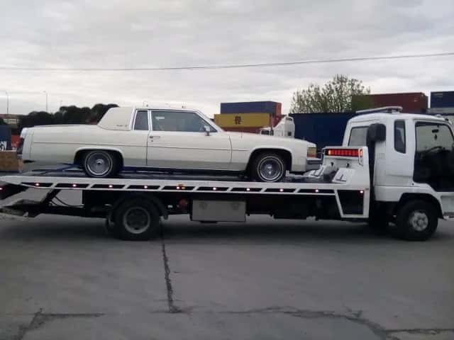 Quokka Towing tilt tray carrying a white classic car past a container yard