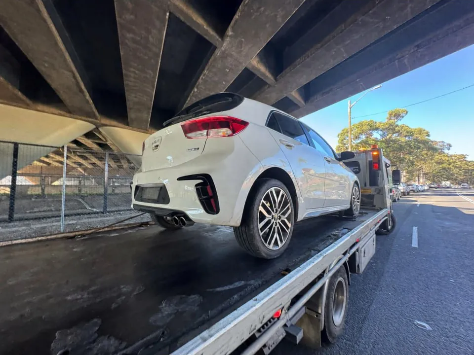 Quokka Towing tilt tray carrying a white hatchback under a rail bridge