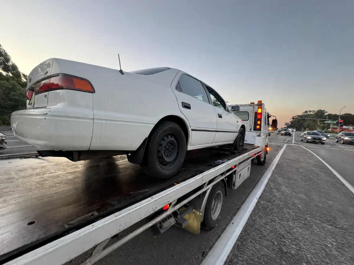 Quokka Towing tilt tray carrying a white sedan on a main road at dusk