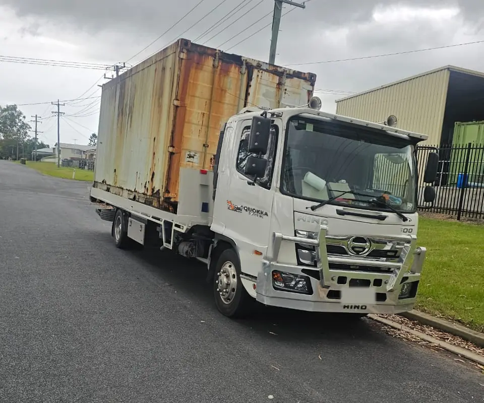 Quokka Towing tow truck carrying a rusted shipping container on a wet street