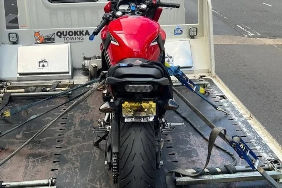 Red sports bike strapped down on a Quokka Towing tilt tray with wheel chock and ratchet straps