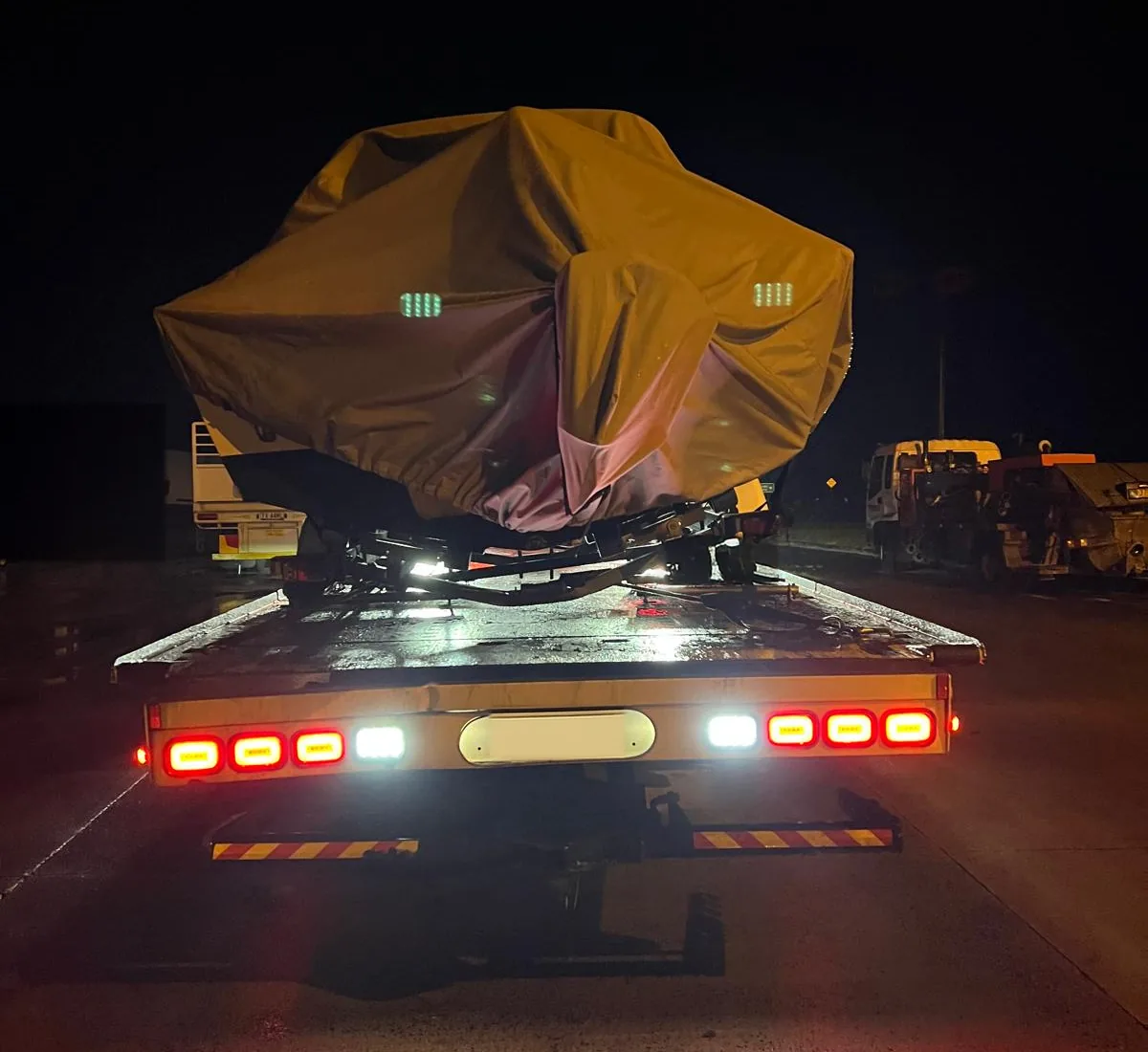 Covered boat on its trailer loaded onto a tilt tray at night