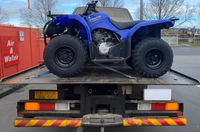 Blue quad bike strapped down on the back of a tilt tray