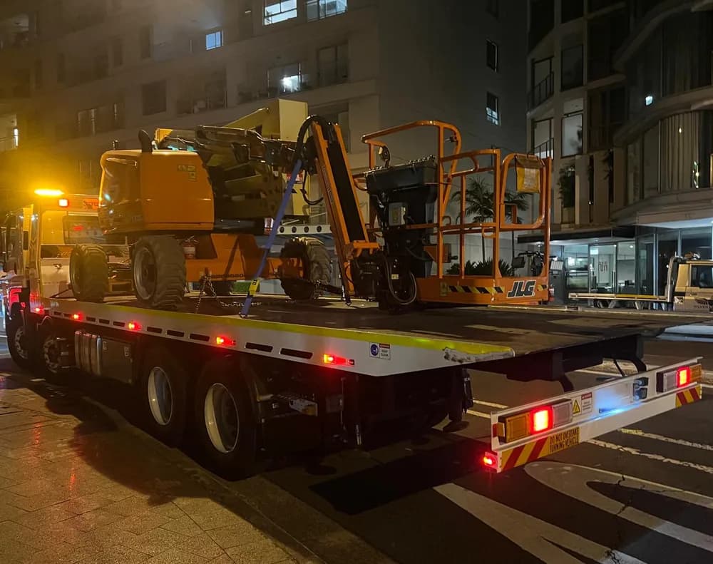 Two elevated work platforms strapped down on a tilt tray at night