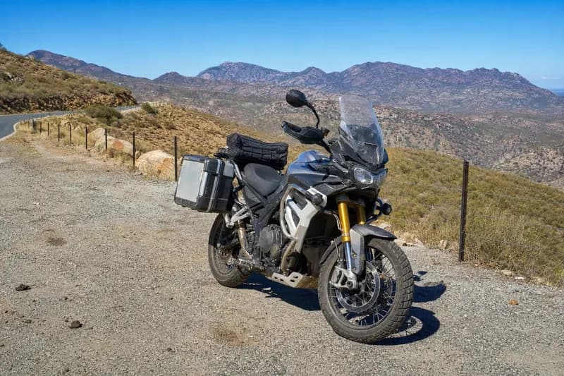 Triumph Tiger adventure motorcycle parked with scenic mountain backdrop.