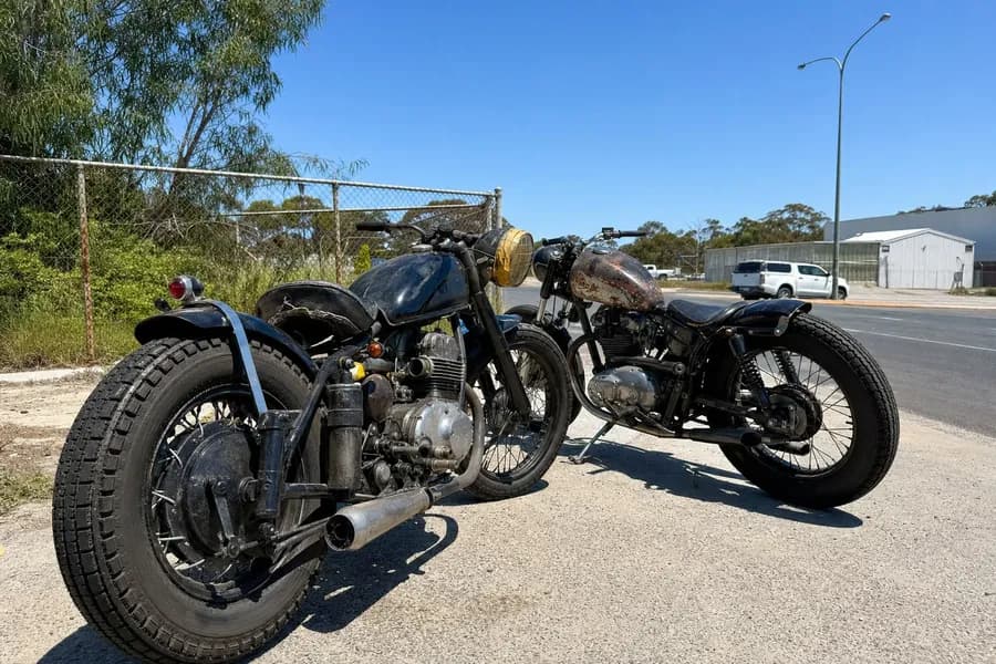 Two vintage motorcycles parked on pavement, one with a taped headlight and custom detailing.